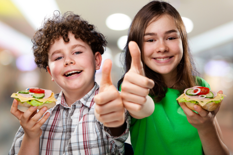 Two teenagers holding sandwiches and making the thumbs-up sign