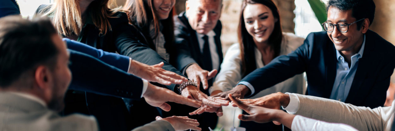 Group of people in an office putting their hands together at the center of a table