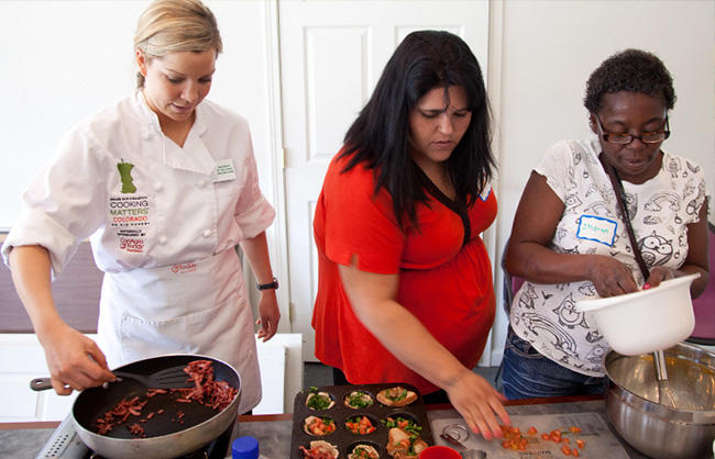 A woman teaching other women how to prepare a meal in a kitchen