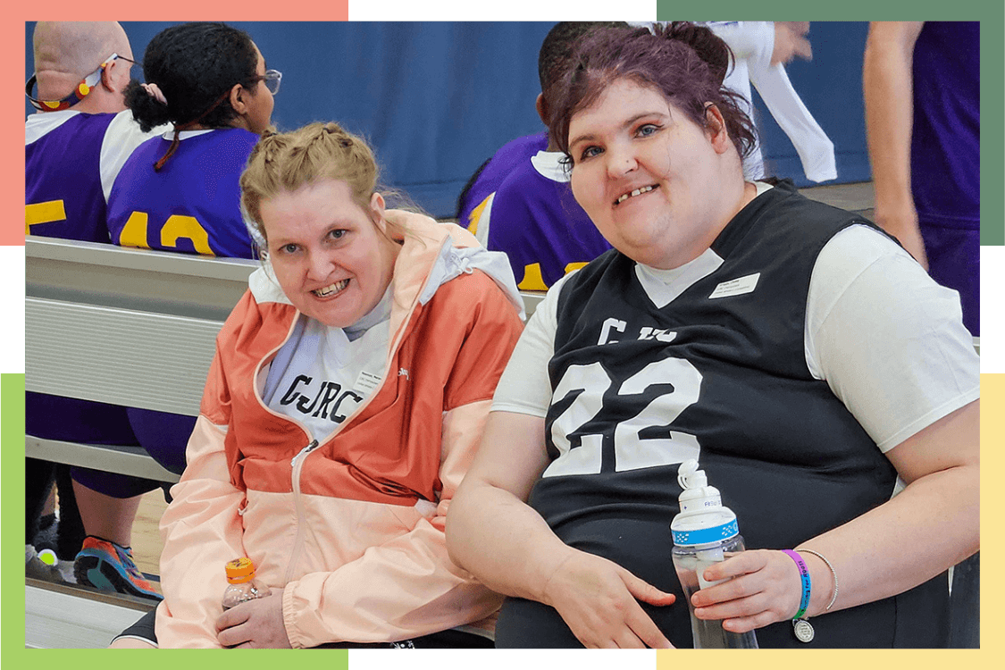 Two female Regional Center residents sit on a bench during a basketball game