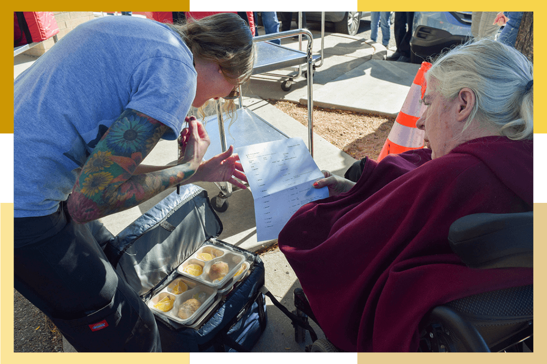 A female Pueblo Regional Center staff member and female resident check over a Meals on Wheels food delivery pickup