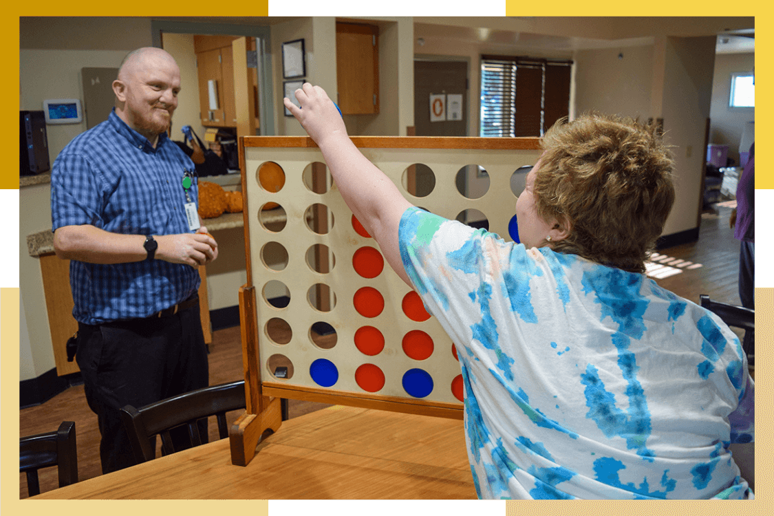 A female Pueblo Regional Center resident plays Connect Four with a male staff member