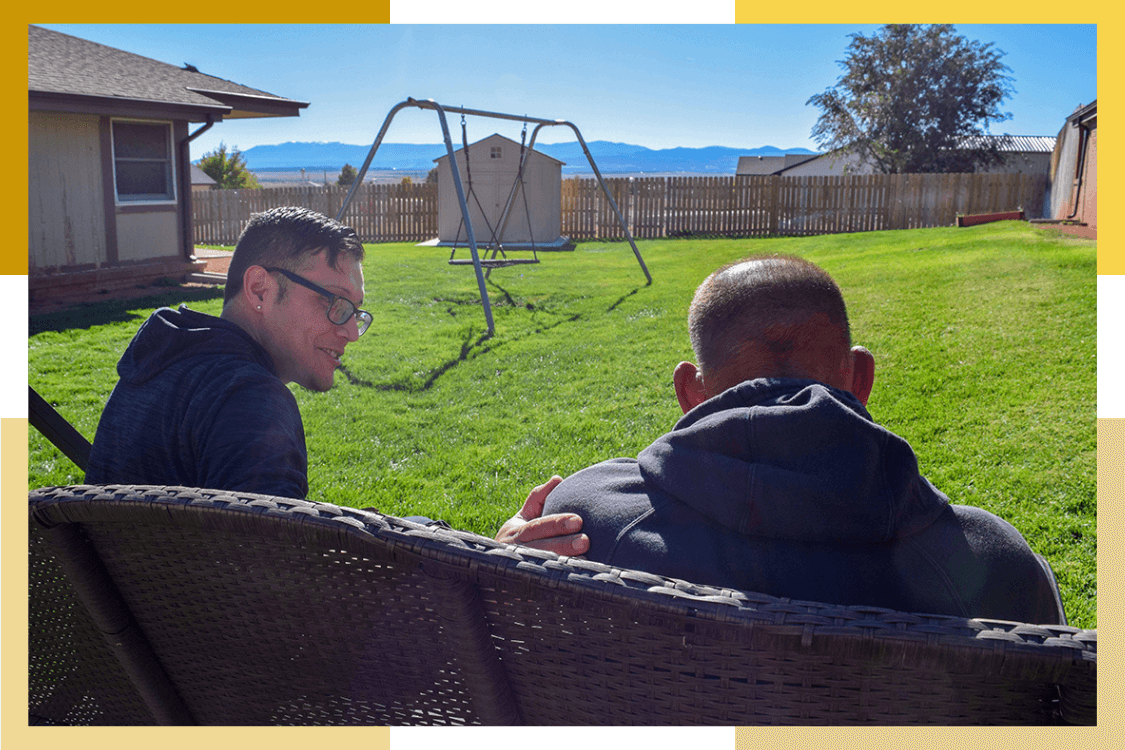 A male Pueblo Regional Center staff member and male resident sit on an outdoor bench