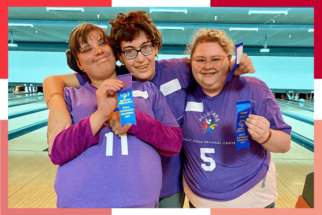 Three female Wheat Ridge Regional Center residents hold up first-place ribbons at a bowling alley