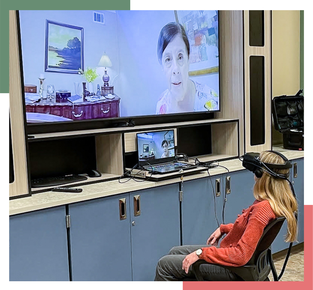 A female Division of Regional Centers staff member wears a virtual reality headset in front of a TV screen showing what the staff member sees.