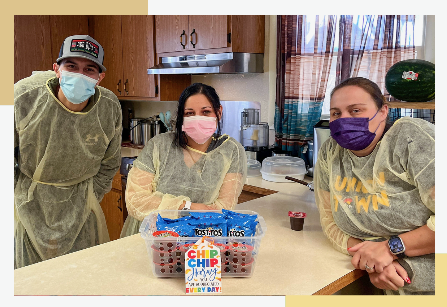 Pueblo Regional Center staff members wear PPE and smile around a plastic container of snacks.