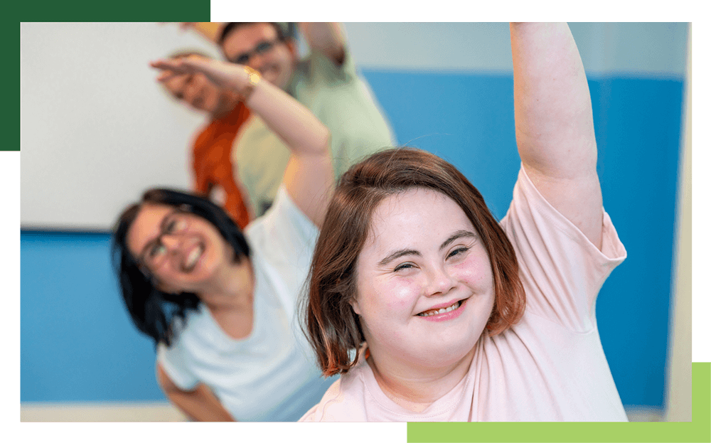 A young woman with IDD stretches with staff stretching behind her