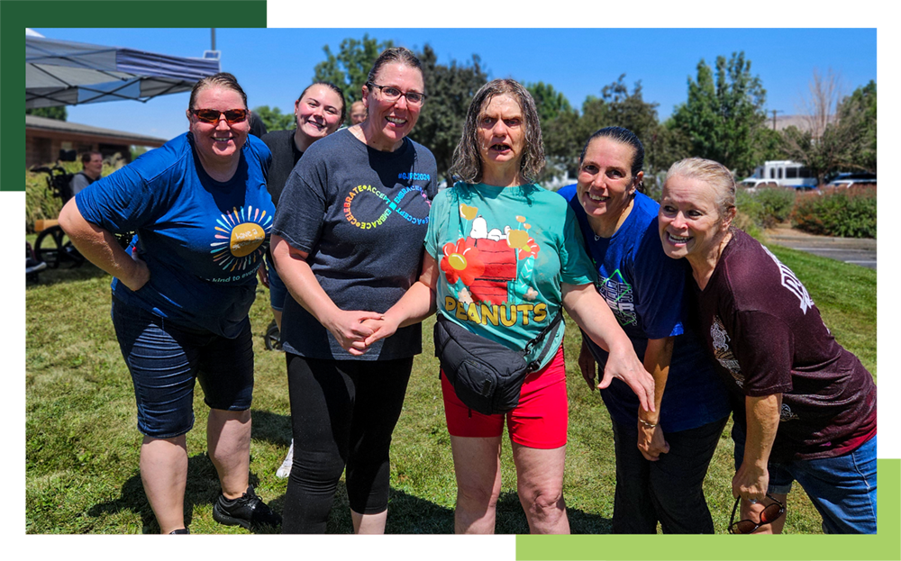 Five female staff members of Grand Junction Regional Center gather around a female individual with IDD during an outdoor water fun event.