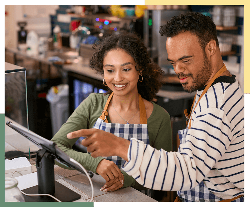 An individual with an intellectual or developmental disability learns how to work a cashier job with the help from a young woman.