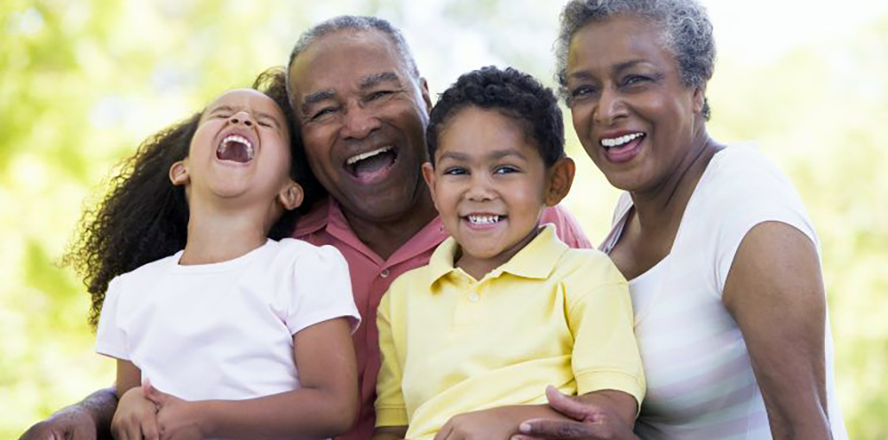 A smiling family of four, including two grandparents and two young grandchildren, is posing for a photo outdoors.