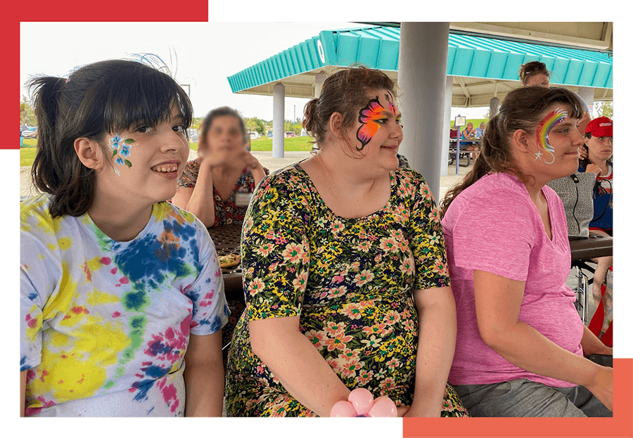 Three young female residents of Wheat Ridge Regional Center show off colorful paintings on their faces.