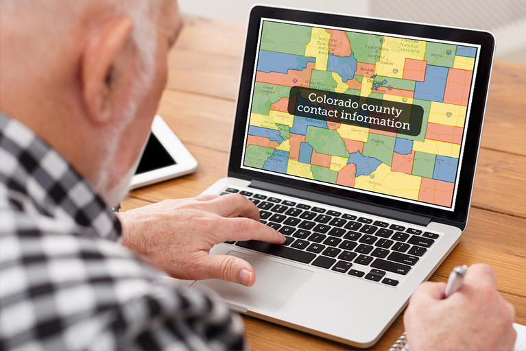 Older man using a laptop with a map of Colorado counties on the screen