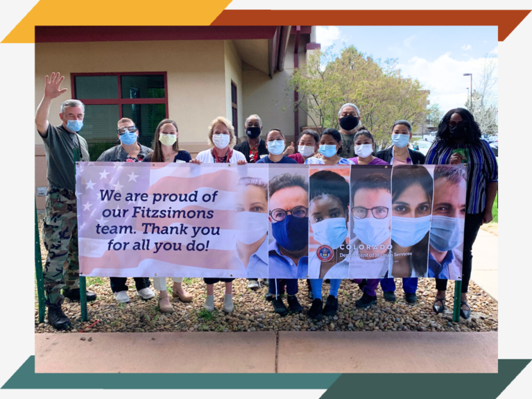 A dozen staff members stand around a sign that reads, "We are proud of our Fitzsimons team. Thank you for all that you do!"