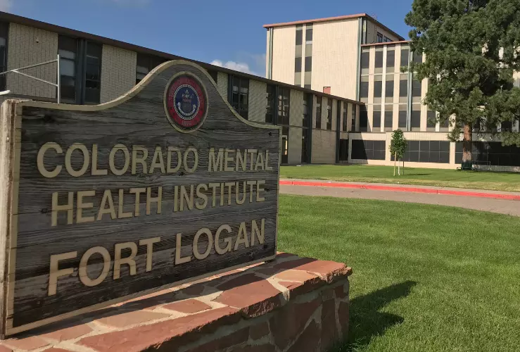 Photo of Colorado Mental Health Hospital in Fort Logan campus, with old sign that says "Colorado Mental Health Institute Fort Logan"